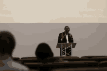 a man stands at a podium with a microphone in front of a screen that says facebook the pastor 's place on it