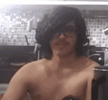 a shirtless man wearing glasses and headphones is sitting in a kitchen .