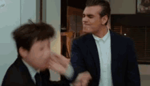 a man in a suit is slapping another man on the face .