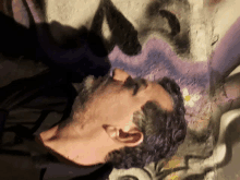 a man with purple hair is laying on his back in front of a graffiti wall