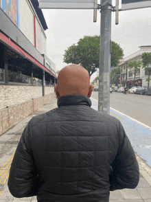 a man in a black jacket is standing on a sidewalk in front of a building that says ' a ' on it