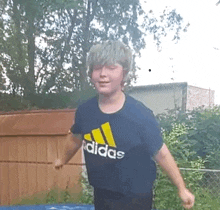 a young boy wearing a blue adidas t-shirt is jumping on a trampoline .