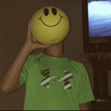 a boy in a green under armour shirt holds a smiley face basketball