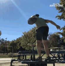 a man is standing on a picnic table with a frisbee in his hand and the words " awesome " on the bottom