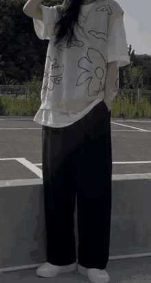 a woman is standing in a parking lot wearing a sweater vest with a flower on it and black pants .