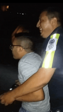 a police officer holds a man in his arms and has a patch on his arm that says ' emergency assistance '