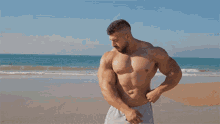 a shirtless man flexes his muscles on a beach