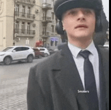 a man in a suit and tie wearing headphones and a hat is standing on a street .