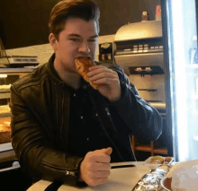 a man in a leather jacket is eating a sandwich in front of a vending machine that says ' americano ' on it