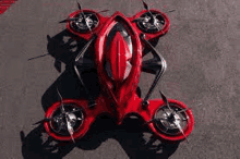 a red flying car with four propellers is sitting on top of a concrete surface .