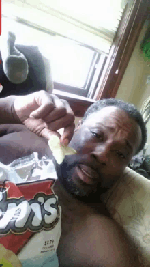 a shirtless man is eating a bag of doritos chips