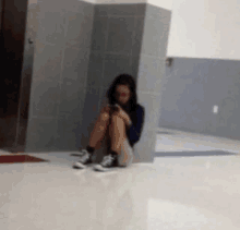 a woman is sitting on the floor in a hallway looking at her cell phone .