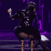 a woman in a black leather jacket is dancing on a stage