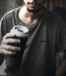 a man in a gray shirt is holding a cup of coffee