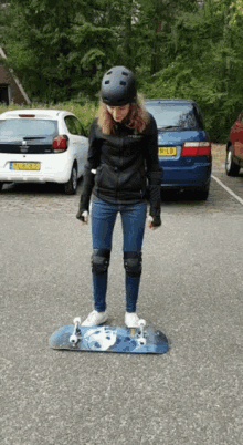 a woman wearing a helmet and knee pads is standing on a skateboard in a parking lot with cars parked behind her