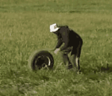 a man is standing in a field with a tire in the grass .