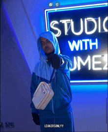 a man in a blue jacket stands in front of a neon sign that says studio with ume