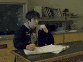 a young man sits at a desk with a book open to a page that says ' emergency exit ' on it