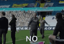 a group of people standing on top of a soccer field with the word no written on the ground .