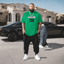 a man wearing a green kick.com t-shirt stands in front of a car