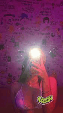 a woman is taking a selfie in front of a purple wall with stickers on it .