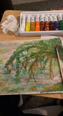 a painting of trees is being painted on a wooden table next to a box of paint