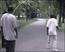 a group of men are walking down a path in a park . one of the men is holding a frisbee .