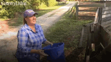 a woman in a plaid shirt is holding a blue bucket in front of a fence that says country living on the bottom