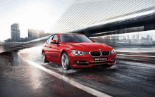 a red bmw 3 series is driving down a wet street