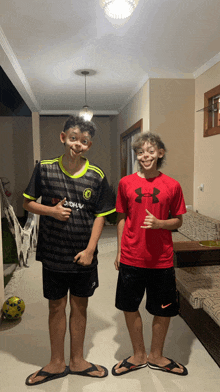 a boy wearing an under armour shirt is standing next to another boy wearing a chelsea shirt