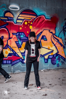 a woman stands in front of a wall with graffiti on it that has the letter a on it