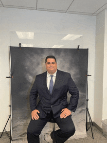 a man in a suit and tie is sitting in front of a black backdrop