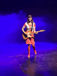 a woman in a red and white polka dot dress is holding a guitar on a stage