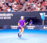 a man in a purple shirt is holding a tennis racquet on a tennis court in front of an emirates banner