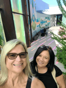 two women are posing for a picture in front of a building with a mural on it