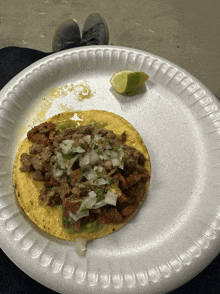 a taco on a styrofoam plate with a lime on it