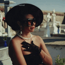 a woman wearing a black hat and gloves is standing in a cemetery with la guarimba film festival written on the top