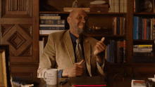 a man sitting at a desk in front of a bookshelf with a mug that says " i am a scientist " on it