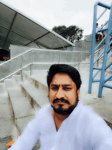 a man in a white shirt is taking a selfie in front of stairs