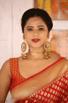 a woman wearing a red and gold saree and earrings