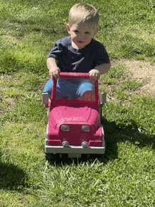 a young boy is sitting in a pink toy truck in the grass