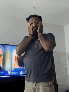 a man covering his ears in front of a tv that has a picture of a man on the screen