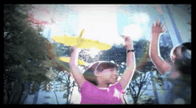 a girl in a pink shirt is holding a yellow toy airplane