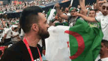 a man in a black shirt with a lanyard around his neck holds a flag in front of a crowd of people