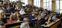 a large group of people are sitting in rows of wooden benches in a lecture hall