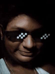 a man wearing sunglasses with a checkered pattern on them is smiling in a dark room .