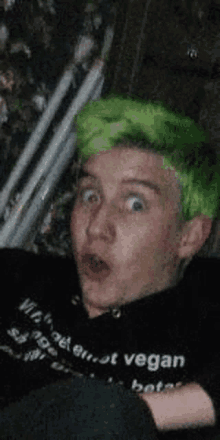 a young man with green hair is wearing a black shirt that says vegan .