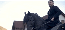 a man is riding a black horse in front of a house with the letters ar on it