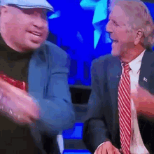 two men in suits and ties are laughing and shaking hands