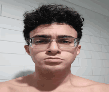 a shirtless man wearing glasses looks at the camera with a serious look on his face